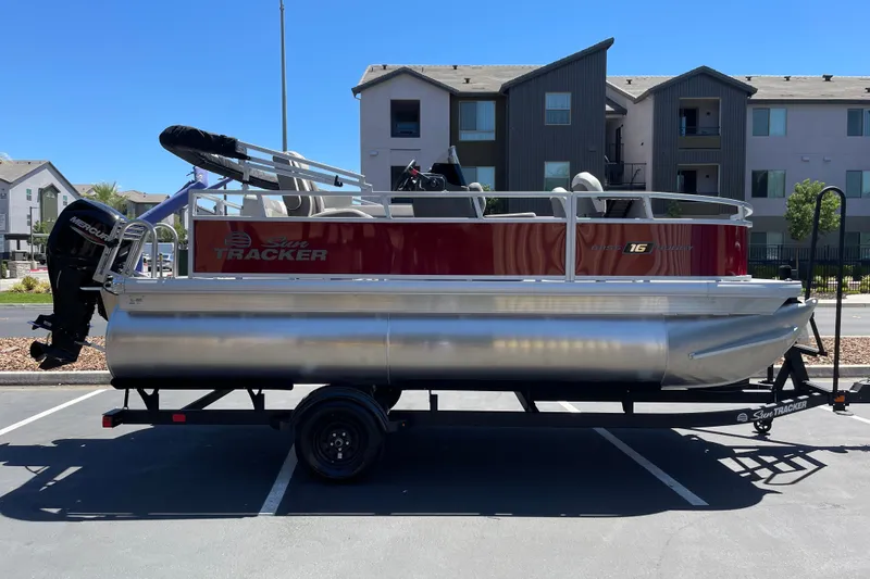 The Image of 2026 Sun Tracker Bass Buggy 16 XL Select pontoon boat on trailer in parking lot. - 0