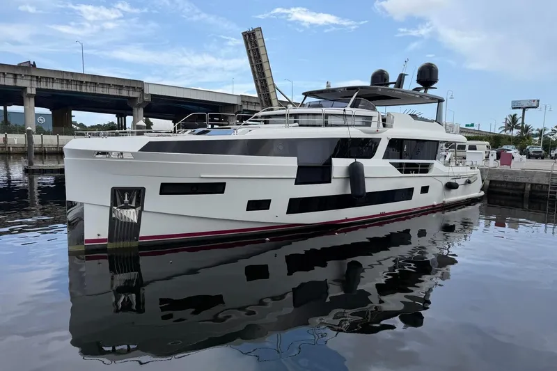 Slide: The Image of 2024 Sirena 88 yacht docked near a bridge, reflecting on calm water. - 1