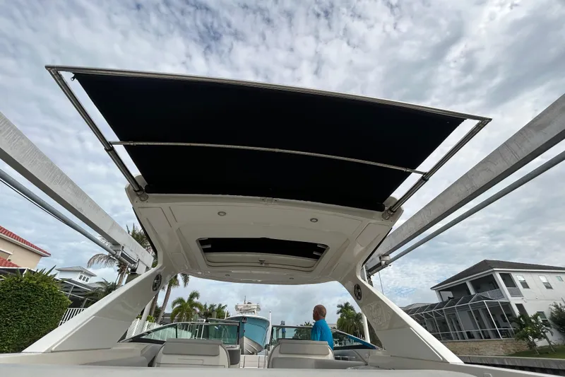 Slide: The Image of 2024 Sea Ray SLX 310 Outboard boat with open canopy, docked near waterfront homes. - 143