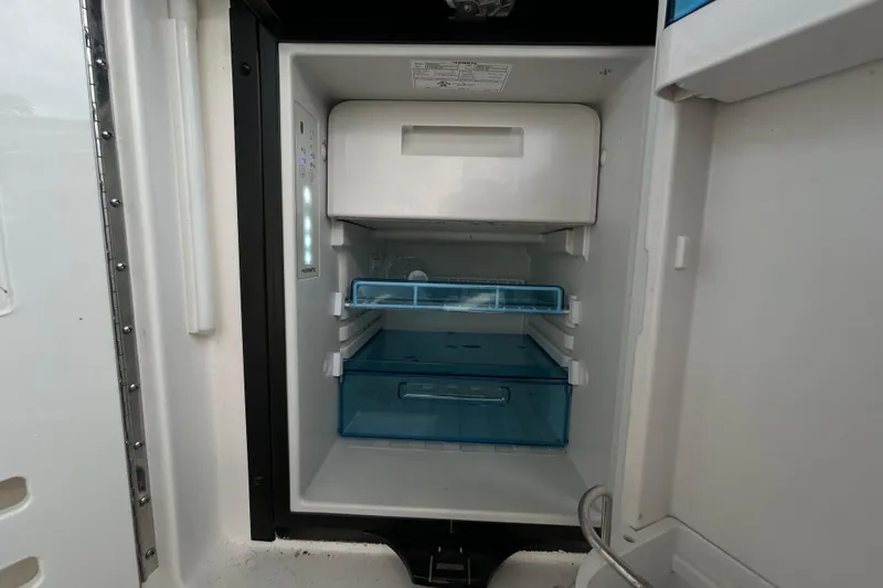 Slide: The Image of Open refrigerator inside 2024 Sea Ray SLX 310 Outboard boat, featuring blue storage drawers. - 48