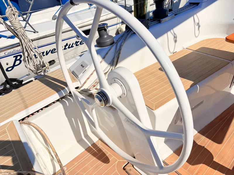 Slide: The Image of A white steering wheel on a sailboat with a wooden deck. - 12