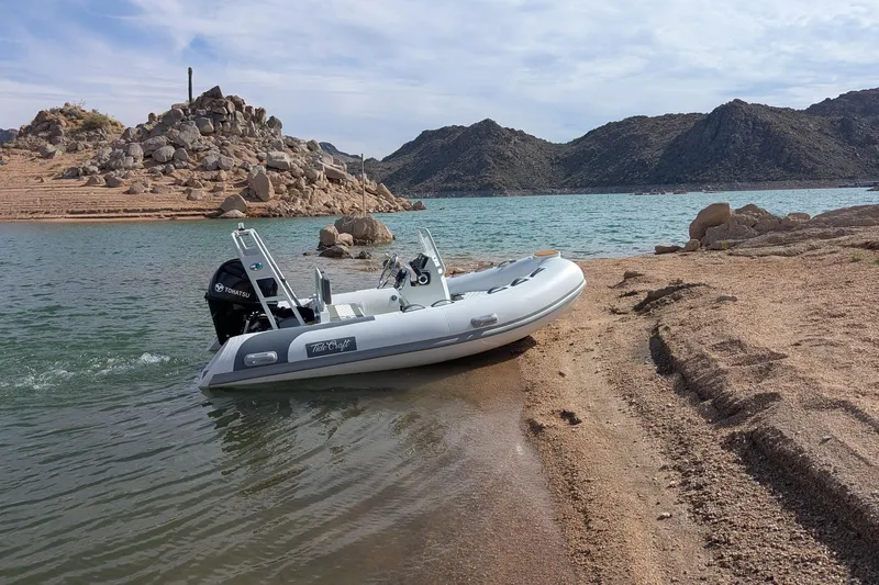 Slide: The Image of Tide Craft San Juan 11 boat on sandy shore, 2027 model, with rocky landscape background. - 18