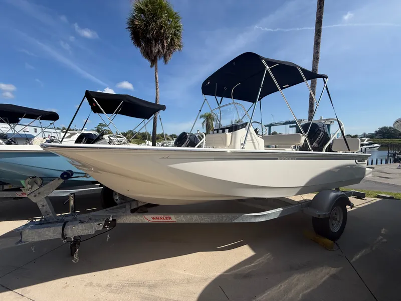Slide: The Image of A 2027 Boston Whaler 170 Montauk on a trailer. It features a sunshade and is parked in a marina area. - 0