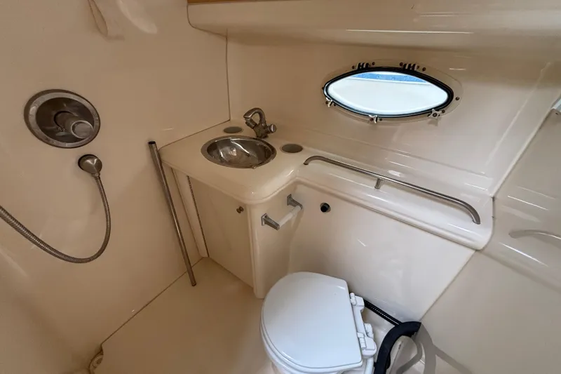 Slide: The Image of 2004 Larson 310 boat bathroom with sink, toilet, and porthole window. - 44