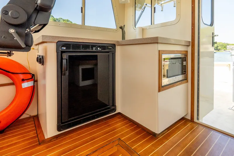 Slide: The Image of Boat interior with compact kitchen, featuring a mini fridge, microwave, and wooden flooring. - 30