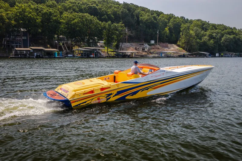 The Image of 2002 Cigarette 35' Playboy Edition speedboat cruising on a lake with lush green shoreline. - 0