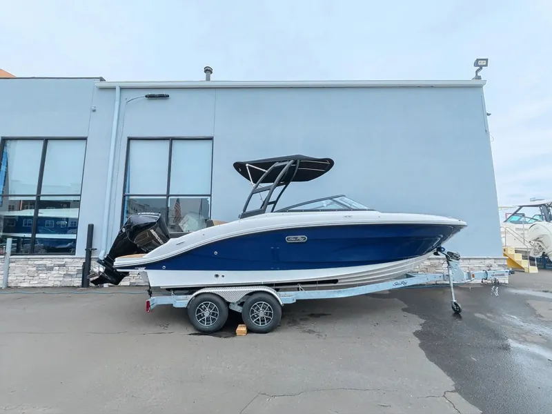 Slide: The Image of Sea Ray SPX 210 Outboard 2027: Blue boat on a trailer, with black canopy, parked by a building. - 1