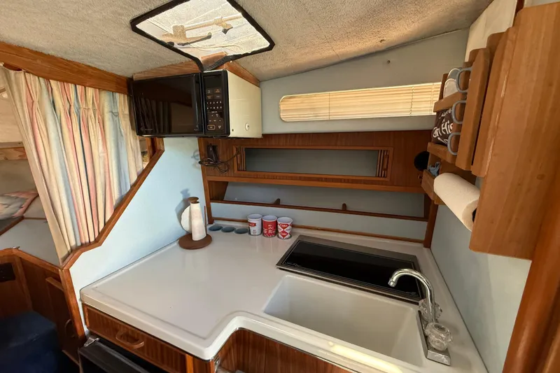 Slide: The Image of 1987 Sea Ray 300 Weekender boat interior kitchen with sink, microwave, and wooden cabinetry. - 10
