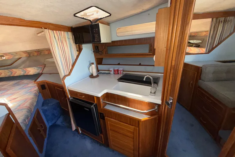Slide: The Image of 1987 Sea Ray 300 Weekender interior with kitchenette, sink, and cozy sleeping area. - 13