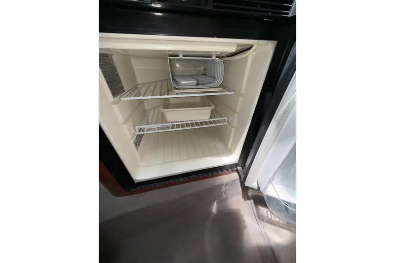 Slide: The Image of Empty refrigerator inside a 2004 Sea Ray 240 Sundancer boat, showing shelves and compartments. - 17
