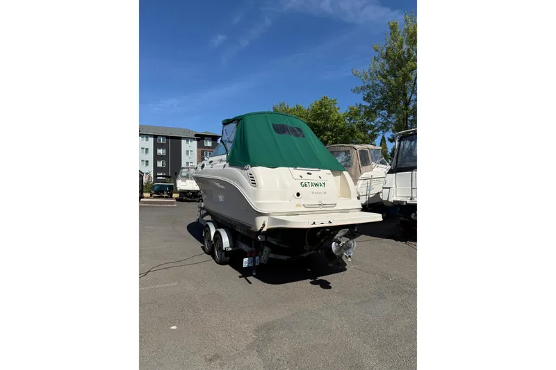 Slide: The Image of 2004 Sea Ray 240 Sundancer boat with green cover on trailer in parking lot. - 2