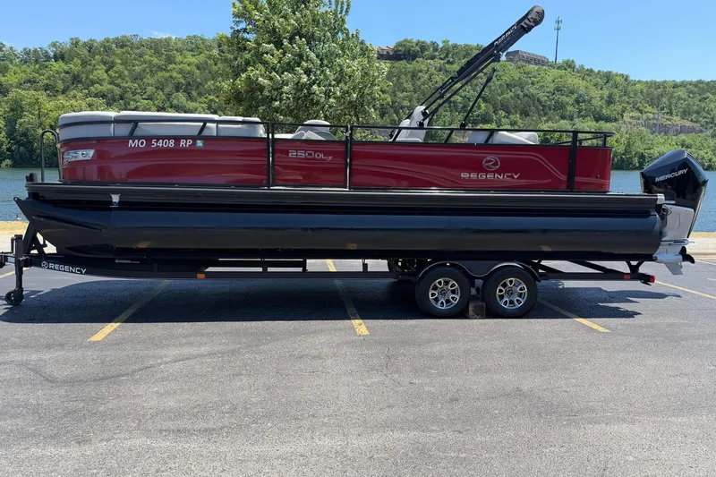 Slide: The Image of 2024 Regency R250DL3 pontoon boat on trailer, parked near a scenic lake. - 3