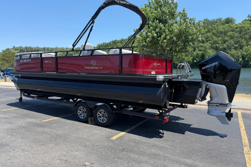 Slide: The Image of 2024 Regency R250DL3 pontoon boat on trailer, parked near a scenic lake. - 7