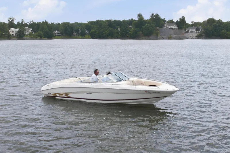 Slide: The Image of 1997 Sea Ray 230 Signature boat cruising on a serene lake under a clear blue sky. - 2