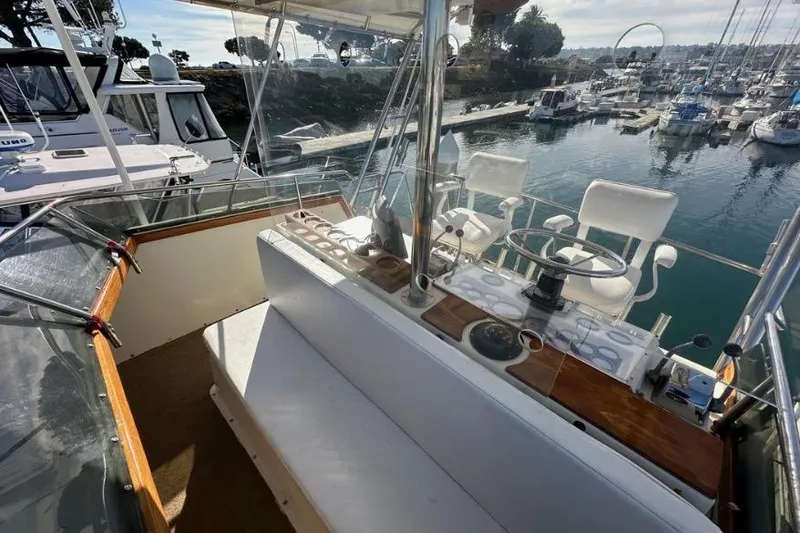 Slide: The Image of 1985 Egg Harbor 33 Sedan yacht helm with marina view, featuring white seating and steering wheel. - 16
