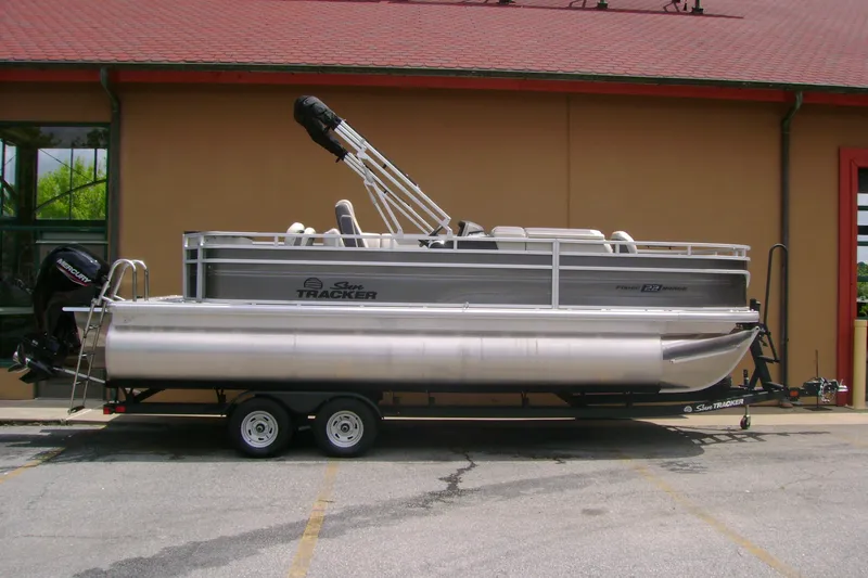 The Image of A 2026 Sun Tracker Fishin' Barge 22 XP3 on a trailer in front of a building. - 0
