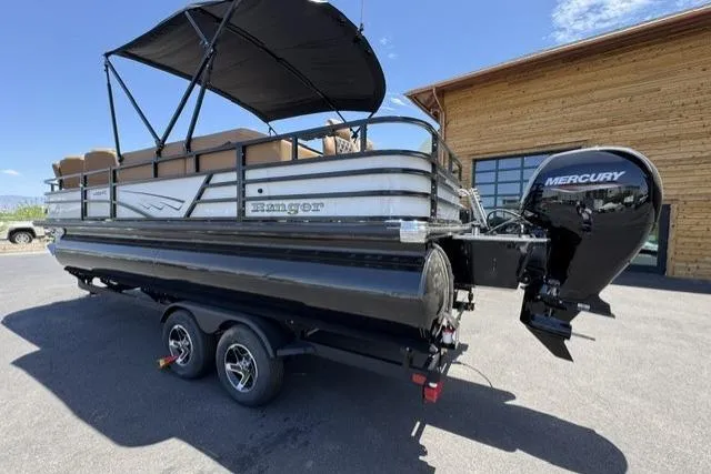 Slide: The Image of 2026 Ranger 220FC pontoon boat with Mercury engine, parked on a trailer outside a wooden building. - 1