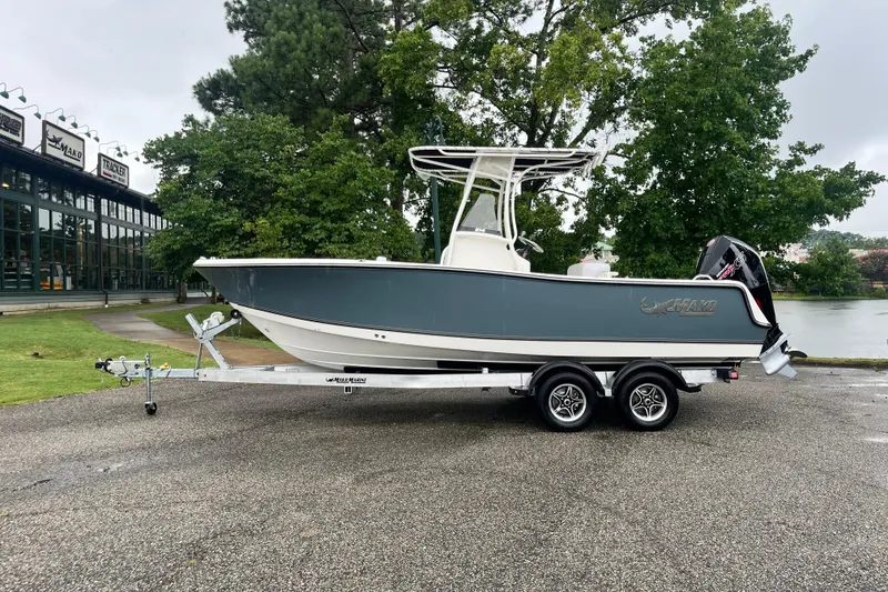 The Image of 2026 Mako 214 Center Console boat on trailer, parked near a lake with trees. - 0