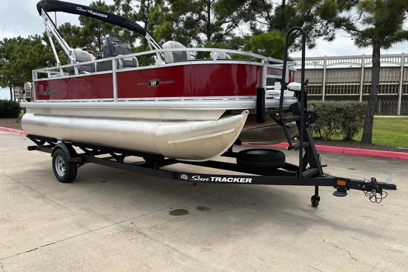 Slide: The Image of 2026 Sun Tracker Bass Buggy 18 DLX pontoon boat on trailer, parked outdoors. - 2