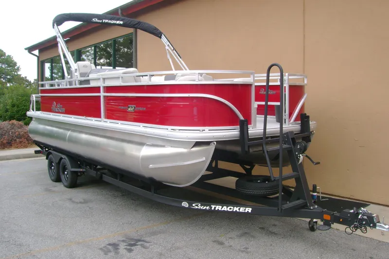 Slide: The Image of 2026 Sun Tracker Fishin' Barge 22 DLX pontoon boat on trailer, parked outdoors. - 1