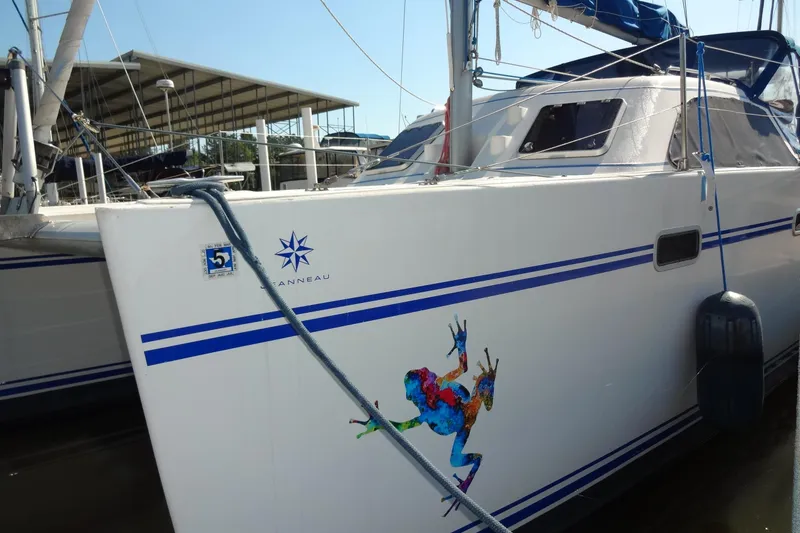 Slide: The Image of 1996 Lagoon 35 CCC catamaran docked, featuring colorful frog artwork and blue stripes. - 70
