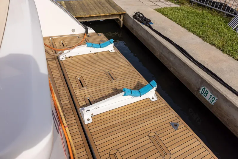 Slide: The Image of 2014 Azimut 54 Flybridge yacht docked, featuring a wooden swim platform and mooring lines. - 96