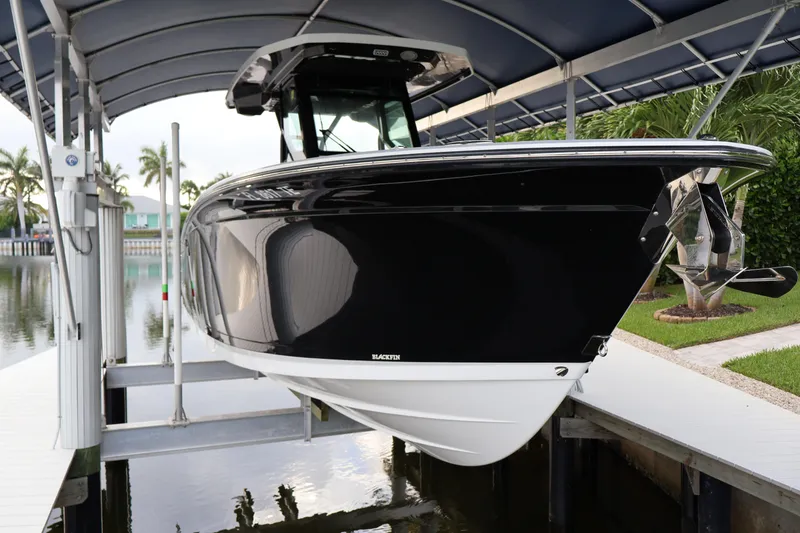 Slide: The Image of 2021 Blackfin 272 CC boat docked under a canopy near a waterfront. - 2