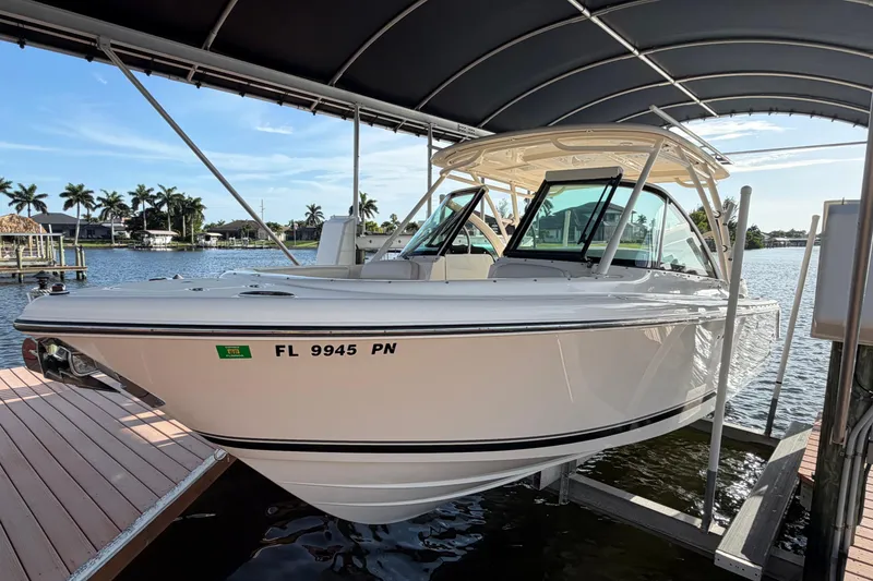 The Image of 2014 Pursuit DC 265 Dual Console boat docked under canopy, sunny waterfront view. - 0