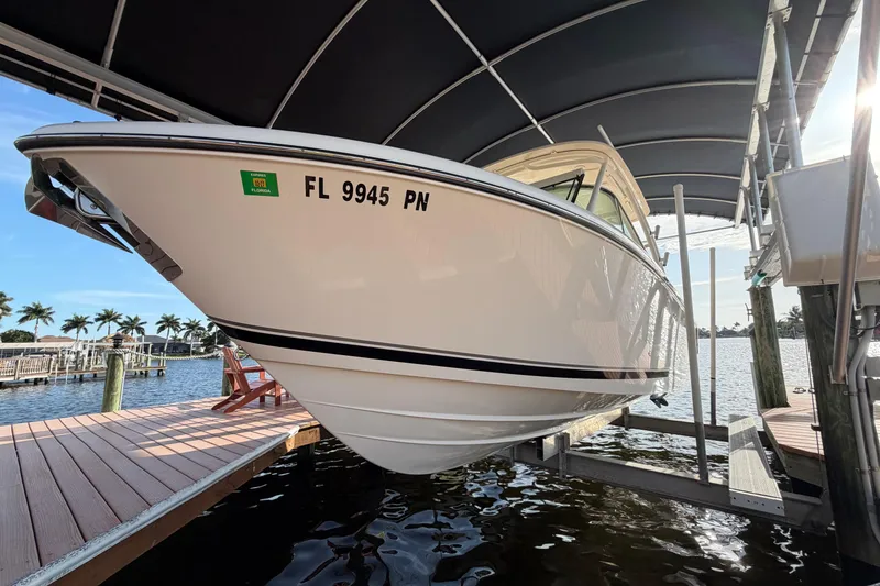 Slide: The Image of 2014 Pursuit DC 265 Dual Console boat docked under a canopy, with water and palm trees in the background. - 3