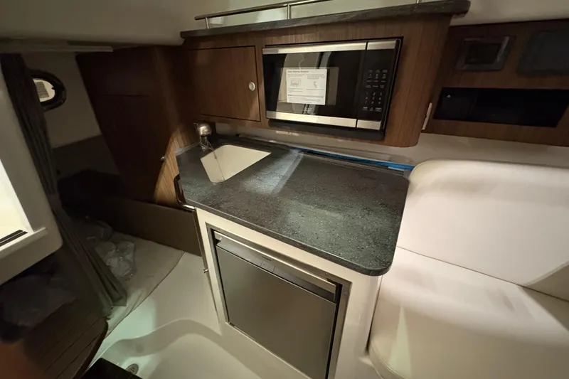 Slide: The Image of 2026 Boston Whaler 285 Conquest interior kitchen with sink, microwave, and compact fridge. - 18
