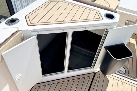 Slide: The Image of 2025 Yamaha Boats 222 FSH Sport E storage compartment with open doors and trash bin. - 24