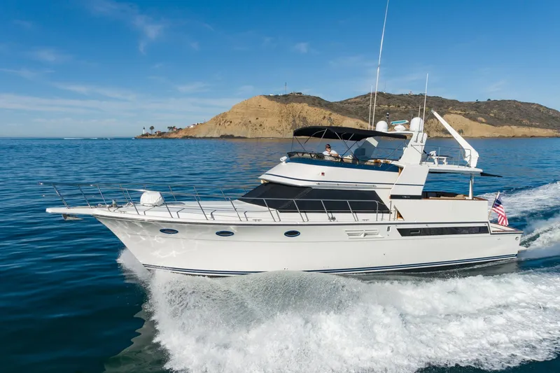The Image of 1991 Californian 55 Cockpit Motor Yacht cruising on blue ocean near rocky coastline. - 1