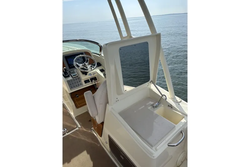 Slide: The Image of 2017 Chris-Craft Calypso 26 helm with steering wheel and sink, overlooking calm waters. - 15