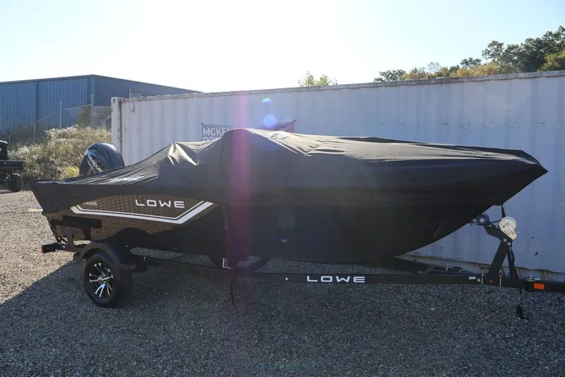 Slide: The Image of 2027 Lowe Fishing Machine 1625SC boat covered, parked on gravel near a container. - 28
