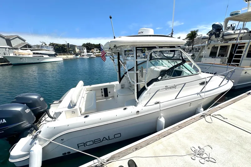 The Image of 2006 Robalo R245 Walkaround boat docked in a marina with twin Yamaha engines. - 0