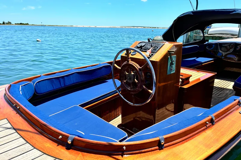 Slide: The Image of 2003 Castine Harbor Launch with blue seating, wooden helm, docked on a sunny day. - 3