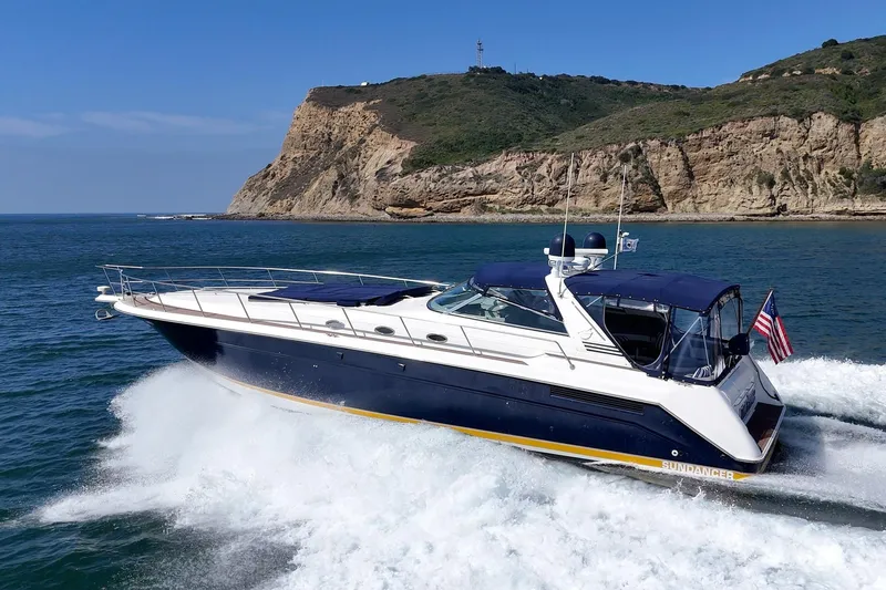 Slide: The Image of 1999 Sea Ray 500 Sundancer yacht cruising near rocky coastline under clear blue sky. - 1