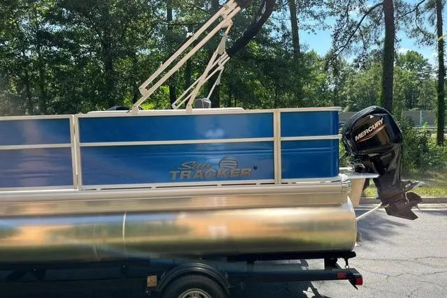 Slide: The Image of 2026 Sun Tracker Party Barge 18 DLX pontoon boat with Mercury outboard motor in a wooded setting. - 4