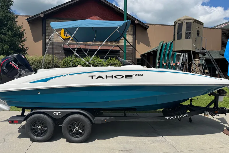 Slide: The Image of 2026 Tahoe 1950 boat with blue canopy on trailer, parked outdoors. - 2