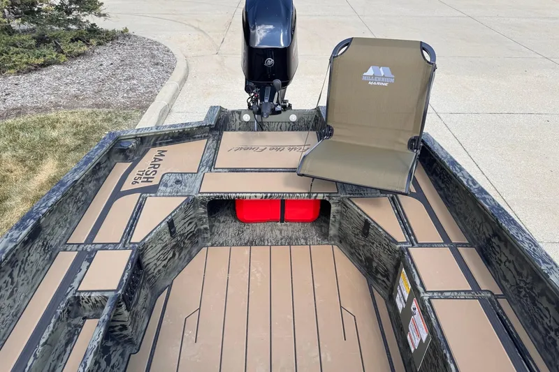 Slide: The Image of 2026 Tracker Grizzly 1756 T Marsh boat interior with seating and motor, parked on pavement. - 4