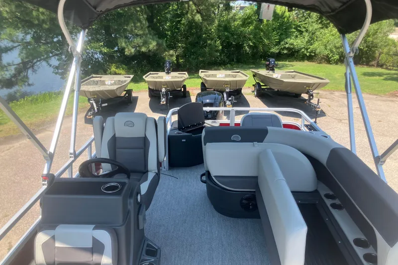 Slide: The Image of 2026 Sun Tracker Bass Buggy 18 DLX interior with seating and steering, parked near small boats. - 7