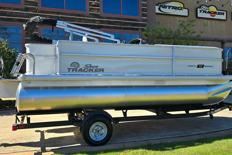 Slide: The Image of 2026 Sun Tracker Party Barge 18 DLX pontoon boat on trailer, parked outdoors. - 2