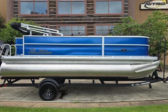 The Image of 2026 Sun Tracker Party Barge 18 DLX pontoon boat on trailer, blue and silver design. - 0