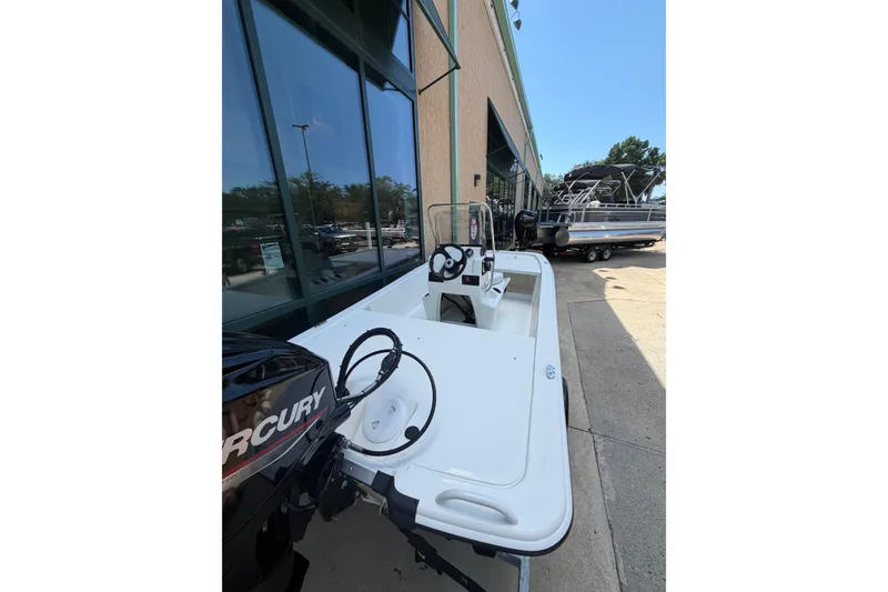 Slide: The Image of 2026 Mako Pro Skiff 13 CC boat with Mercury engine, parked outside a building. - 2