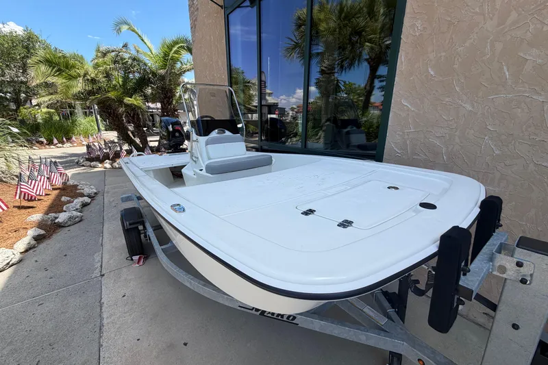 Slide: The Image of 2026 Mako Pro Skiff 13 CC boat on trailer, parked near palm trees and flags. - 1