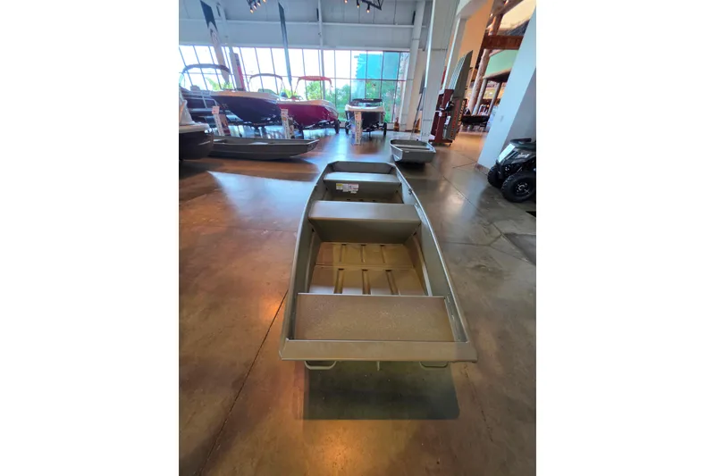 Slide: The Image of 2026 Tracker Grizzly 12 Jon boat displayed in a showroom with other boats. - 2