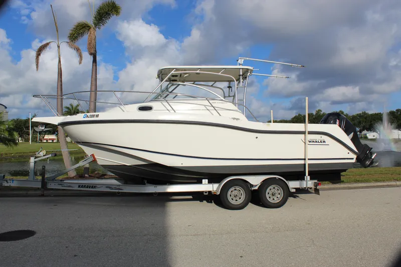 Slide: The Image of 2005 Boston Whaler 255 Conquest boat on trailer, parked near palm trees and water fountain. - 2