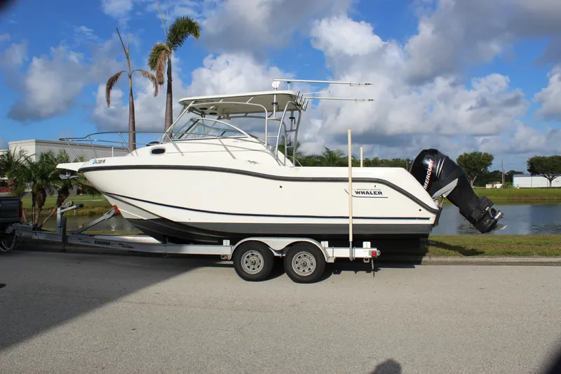 Slide: The Image of 2005 Boston Whaler 255 Conquest boat on trailer, parked near water, under blue sky. - 5
