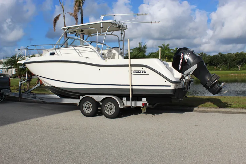 Slide: The Image of 2005 Boston Whaler 255 Conquest boat on trailer, parked near a scenic waterway. - 6
