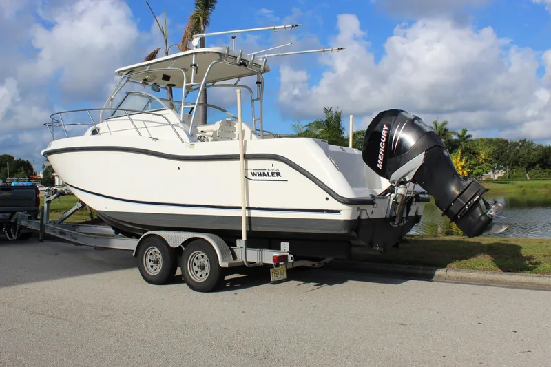 Slide: The Image of 2005 Boston Whaler 255 Conquest boat on trailer, parked near a lake under a blue sky. - 7